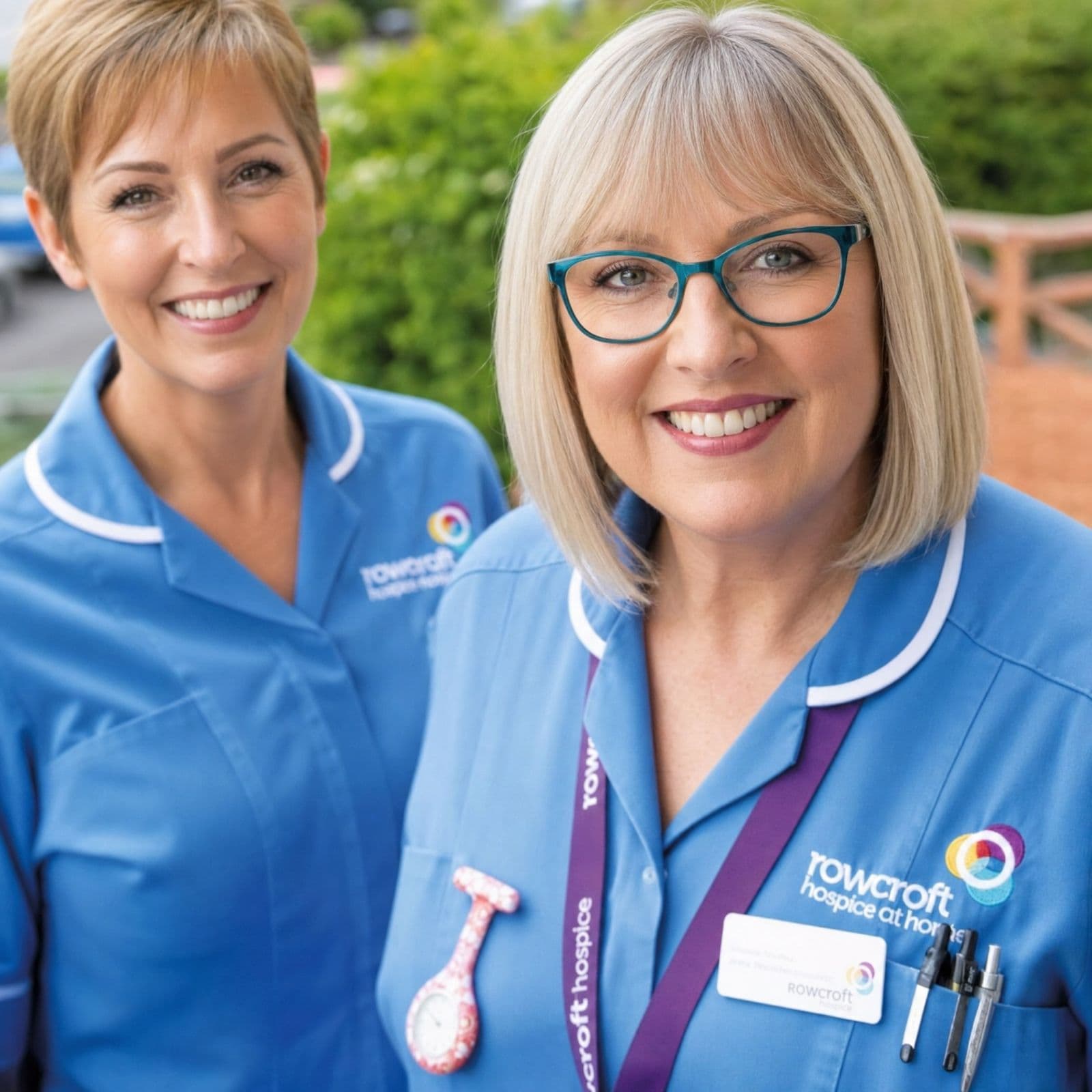 Two care staff in blue Rowcroft Hospice uniforms embroidered with the charity logo